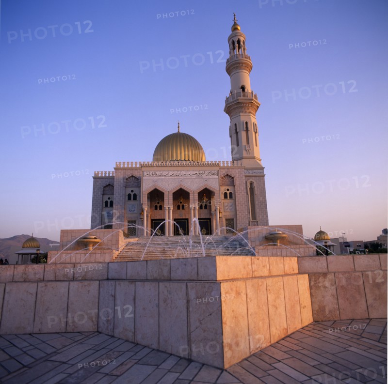 OMAN, Capital Area, Al Khuwair, Zawawi Mosque. Exterior seen at dusk with gold dome shining and fountain in the foreground.
