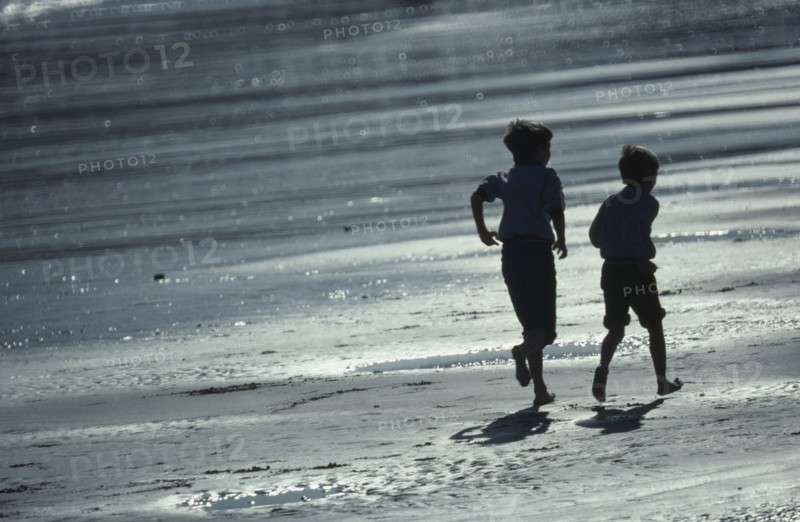 ENGLAND, East Sussex, Hastings, Two boys running along the wet sand of the beach