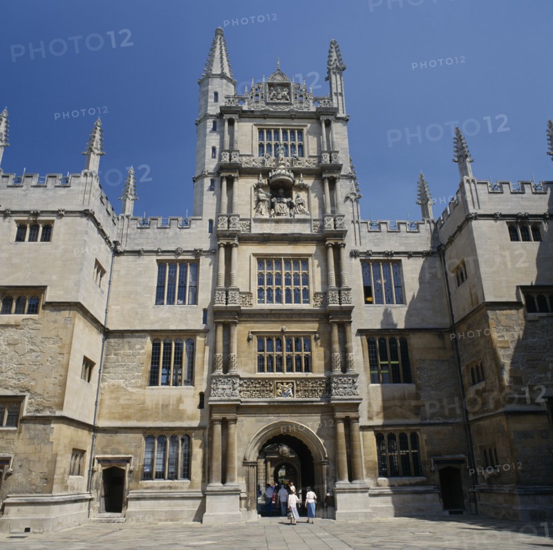 ENGLAND, Oxfordshire, Oxford, The Old Bodleian Library exterior facade with people walking through arched entrance to interior courtyard.