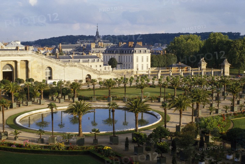 FRANCE, Ile de France, Versailles, General view over round pool surrounded by palms with the town behind