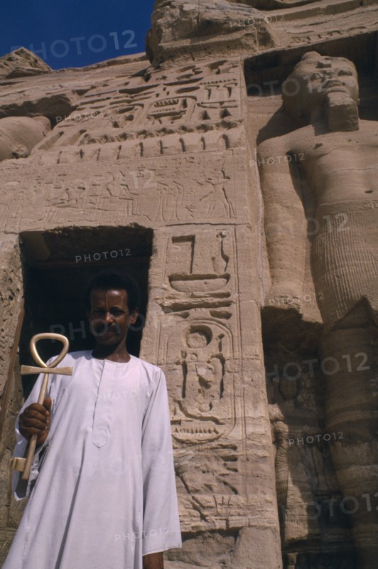 EGYPT, Abu Simbel, Man holding key of life in front of temple statue and hieroglyphics