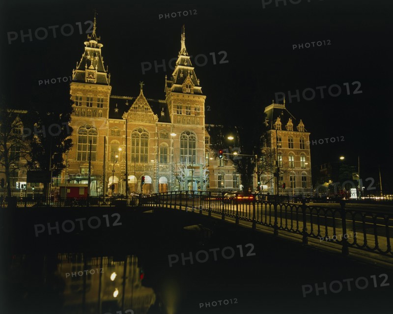 HOLLAND, North, Amsterdam, Rijksmuseum illuminated at night beyond a bridge over a canal reflected in the water