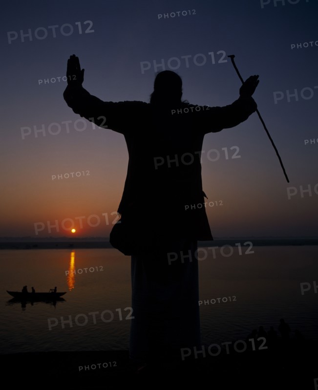 INDIA, Uttar Pradesh, Varanasi, Silhouette at sunset of a Holy Man on the banks of the River Ganges with his arms outstretched