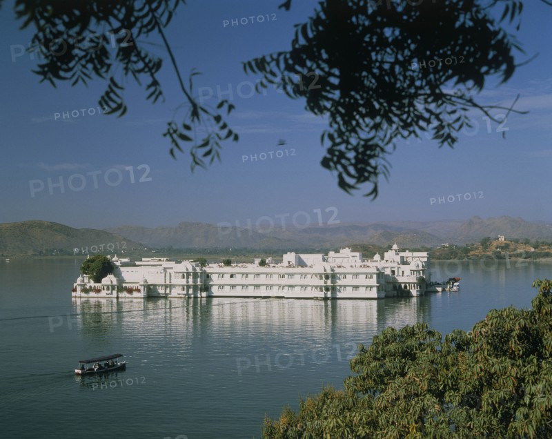 INDIA, Rajasthan, Udaipur, The Lake Palace in the middle of the lake with a covered boat making its way across the water