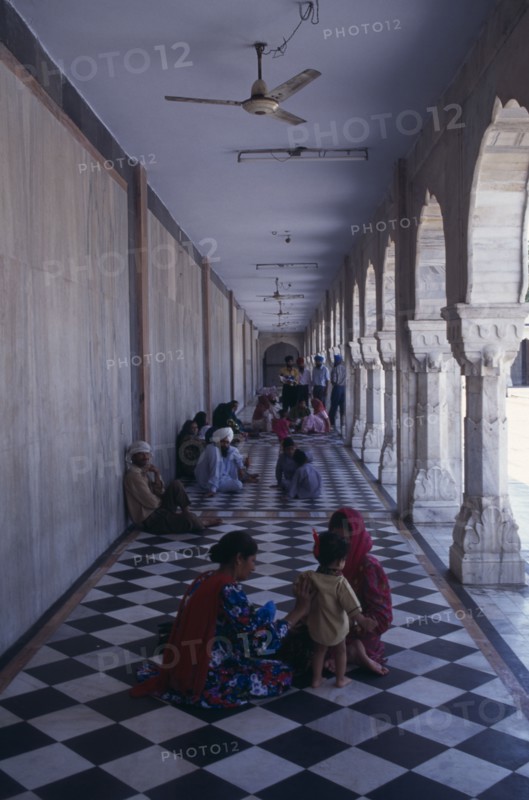 INDIA, Delhi, "Sikh pilgrims sitting on long, colonnaded temple passage-way with black and white chequered pattern floor."