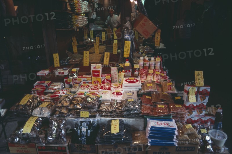 JAPAN, Honshu, Tokyo, Ueno. Display of goods spilling out on to the street from a shop under an archway with the vendor standing inside