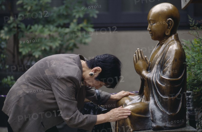JAPAN, Religion, Woman praying before a seated Buddha
