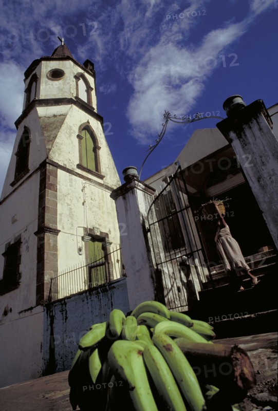 WEST INDIES, Dominica, Roseau, The Methodist Church with Harvest Festival Offering of bananas on the pavement as woman leaves the church
