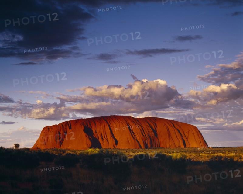 AUSTRALIA, Northern Territory, Uluru, Ayers Rock.  Giant red rock formation at dusk overshadowed by storm clouds