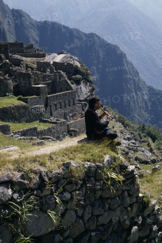 PERU, Cusco, Machu Picchu , Piper sitting at the ruined city playing the flute   Cuzco