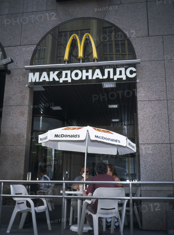 RUSSIA, Moscow, McDonalds Restaurant with people sitting at table and chairs with umbrella outside entrance with restaurant sign in Russian