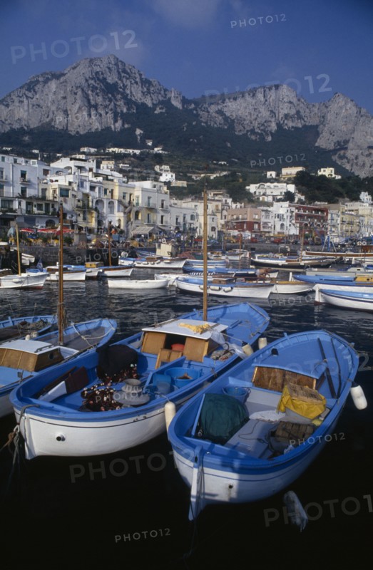 ITALY, Campania, Capri, Marina Grande harbour with fishing boats moored in front of buildings with mountains rising behind them