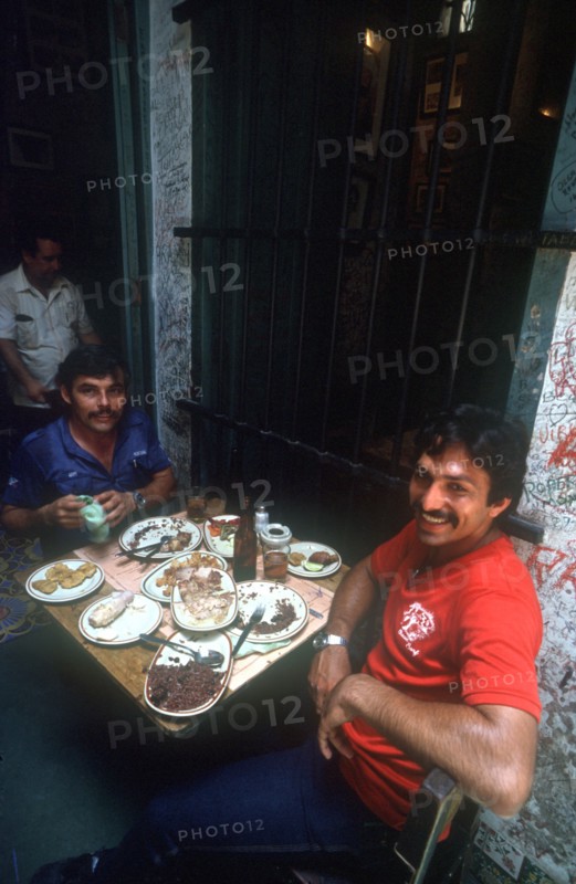 CUBA, Havana, "Bodequita del Medio Bar with two men sitting at a table covered in semi finnished plates of rice, beans and meat"