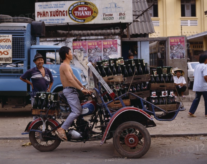 VIETNAM, South, Ho Chi Minh City, Man riding motorbike laden with beer bottles.  Advertising posters