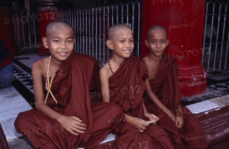 MYANMAR, Yangon, Shwedagon Pagoda, Three young monks sitting on the floor at the front of the temple