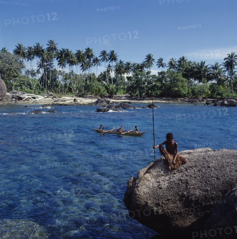 INDONESIA, Irian Jaya, Sorong, Children in outrigger canoe near beach with boy on rock