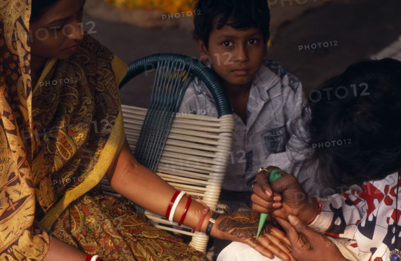 INDIA, Religion, Hindu, Woman having the palms of her hands decorated in Henna for her wedding with small boy onlooking