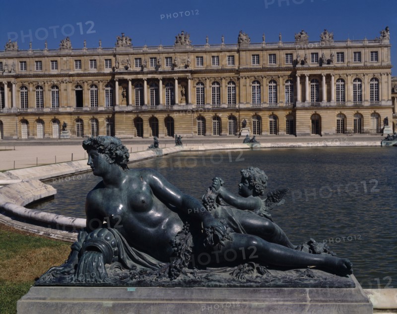 FRANCE, Ile de France, Yvelines, Versailles. Part view of palace with bronze reclined statue of woman with child next to pond