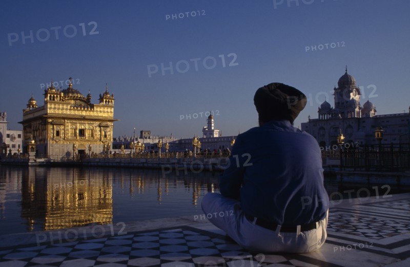 INDIA, Punjab, Amritsar, Golden Temple with pilgrim sat beside sacred pool in the foreground.