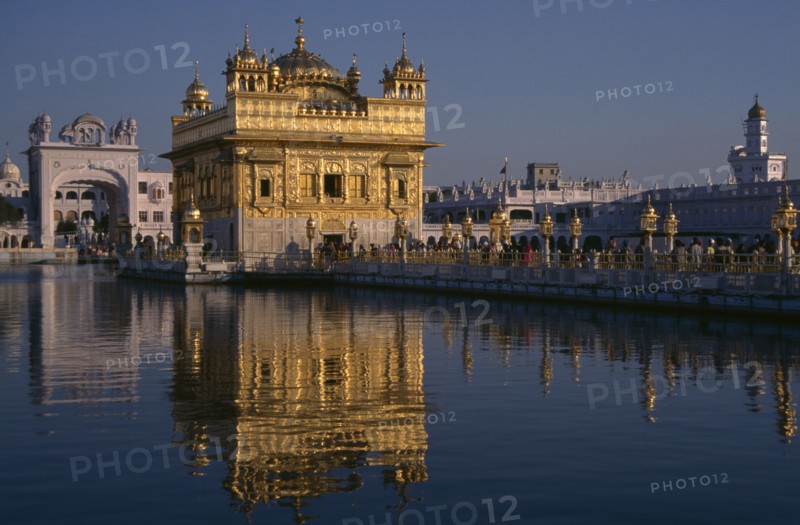 INDIA, Punjab, Amritsar, Golden Temple with pilgrims and visitors on causeway or the Guru’s Bridge leading to temple reflected in rippled surface of pool.