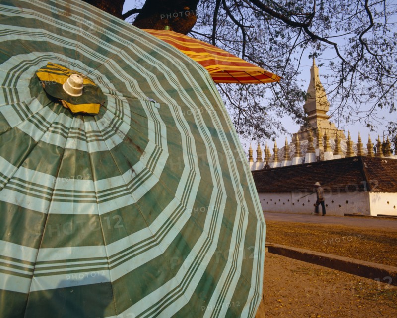 LAOS, Vientiane, Pha That Luang Sacred Stupa with large green striped umbrella in foreground.