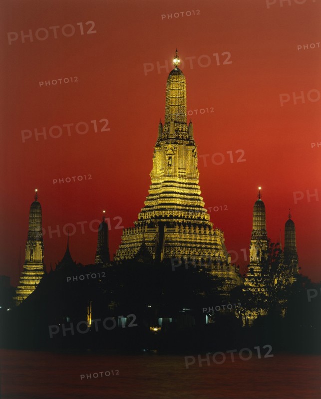 THAILAND, Bangkok, Wat Arun Temple Of The Dawn illuminated at sunset with orange sky and river in foreground