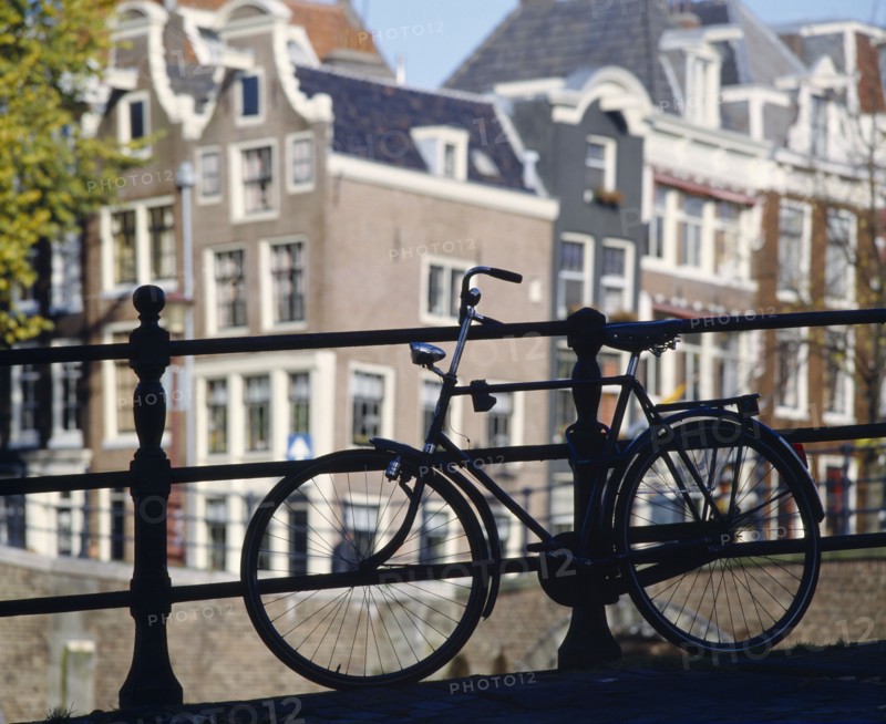 HOLLAND, North, Amsterdam, Bike parked against railings with traditional architecture behind.