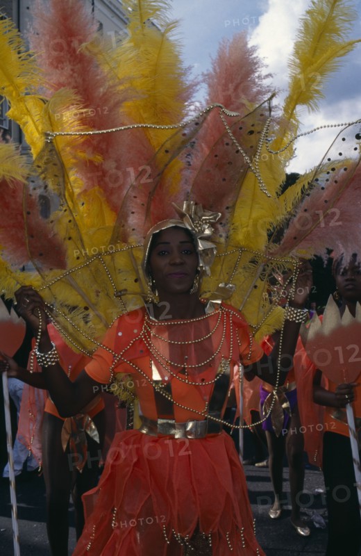 ENGLAND, London, Notting Hill Carnival. Woman in orange costume with orange and yellow feathers and gold head-dress.