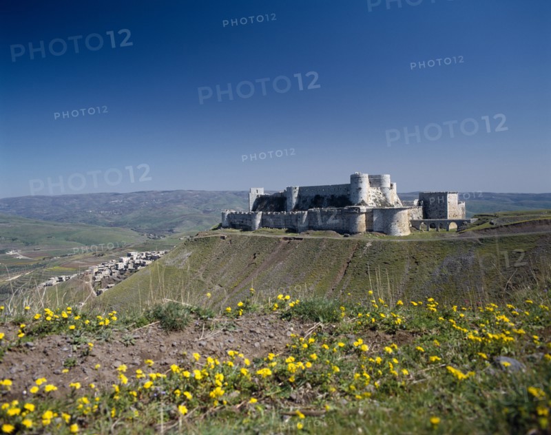 SYRIA, Central, Crac des Chevaliers, Crusader Castle in distance on plateau with village partly seen below