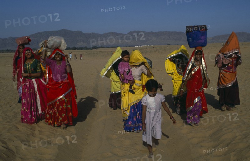 INDIA, Rajasthan, Pushkar, Brightly dressed Rajasthani women and children carrying loads on their heads.