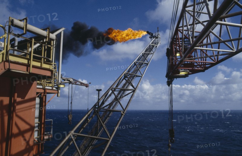 INDUSTRY, Factory, Oil Rig, Burning Off Gas. View along long pipe structure jutting out over the North sea to flames burning at the end