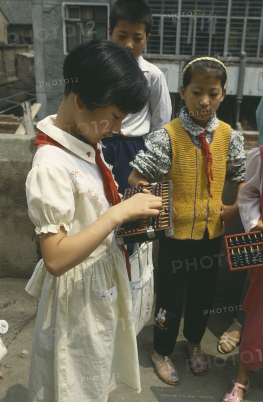 CHINA, Shaanxi, Xian, Schoolgirl standing with other children using an abacus.