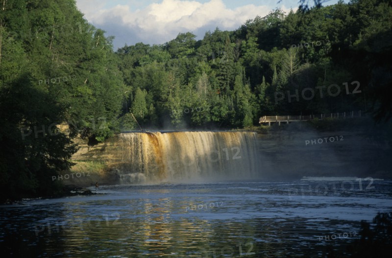 USA, Michigan , Chippewa, Tahquamenon Falls waterfall surrounded by lush greenery and man standing on riverbank nearby