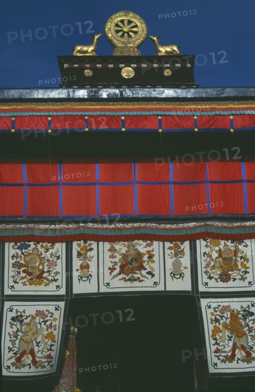 TIBET, Lhasa, Jokhang Temple, Golden Wheel of Dharma on roof of building covered in hanging fabrics with religious images
