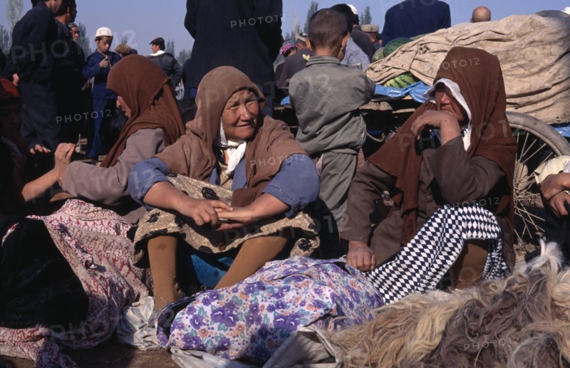 CHINA, Xinjiang, Kashgar, Women sitting with bundles of clothing at the Sunday Market