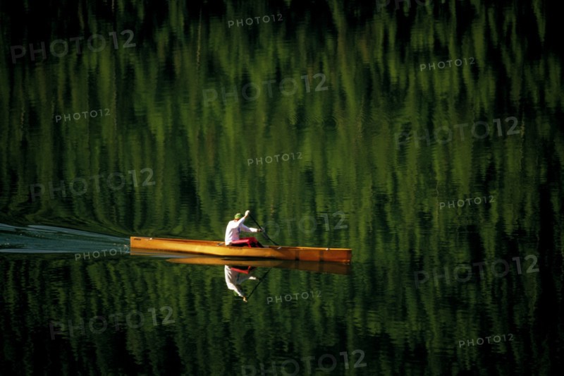 USA, Montana, Salmon Lake, Single canoeist on lake with reflection of trees in the water near Kalispell