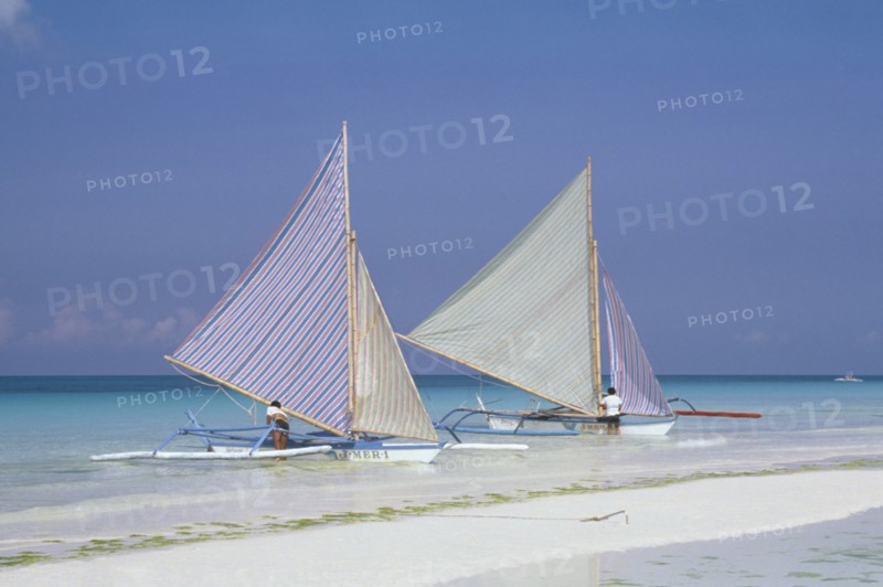 PHILIPPINES, Visayan Islands, Boracay Island, Two outriggers with striped sails moored on the edge of a sandy beach