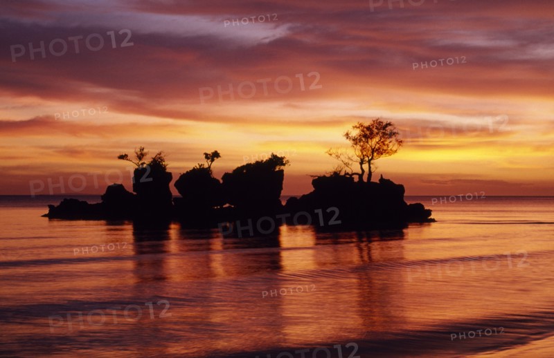 PHILIPPINES, Visayan Islands, Boracay Island, Rocky outcrop with trees just off shore silhouetted against dramatic sunset