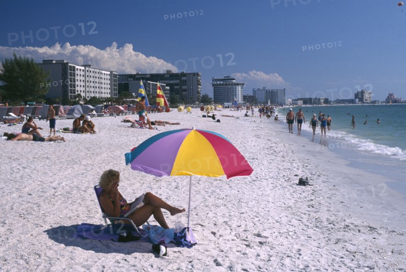 USA, Florida, St.Petersburg , Sunbathers on a golden sandy beach with a yellow parasol and sailboats along the beach behind