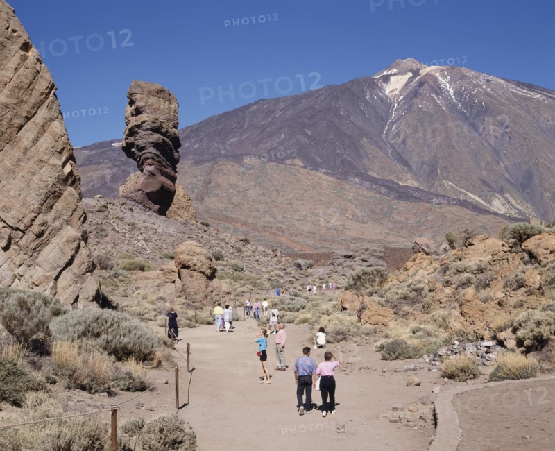 SPAIN, Canary Islands, Tenerife, Mount Teide National Park with tourists on dry and dusty path amongst rock formations with Teide in the distance