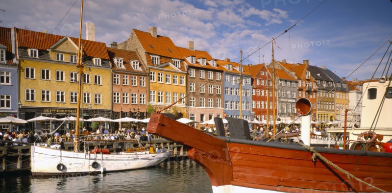 DENMARK,  , Copenhagen, Boats on Nyhavn Canal with pavement cafes and waterside buildings behind.