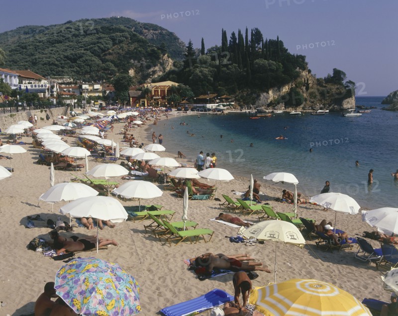 GREECE, Epirus Region, Parga, "Krioneri Beach, view along busy beach with umbrellas and sun loungers to rocky headland"