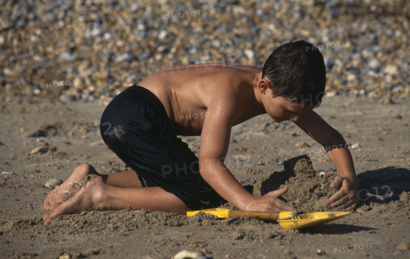 CHILDREN, Playing, Beach, Boy on pebbly & sandy beach making a sand castle