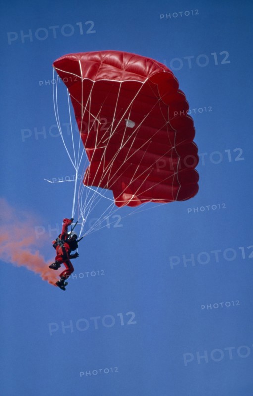 20003695 SPORT Air Parachuting Parachutist with red garments  red Parachute and with red smoke coming from his boots.