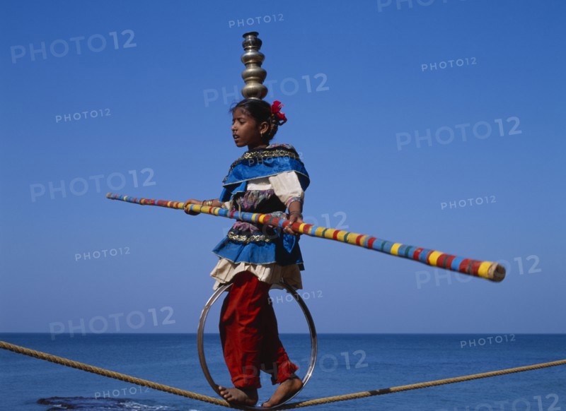 INDIA, Goa , General, "Young girl walks the tightrope while balancing silver pots on her head, blue sky in background"