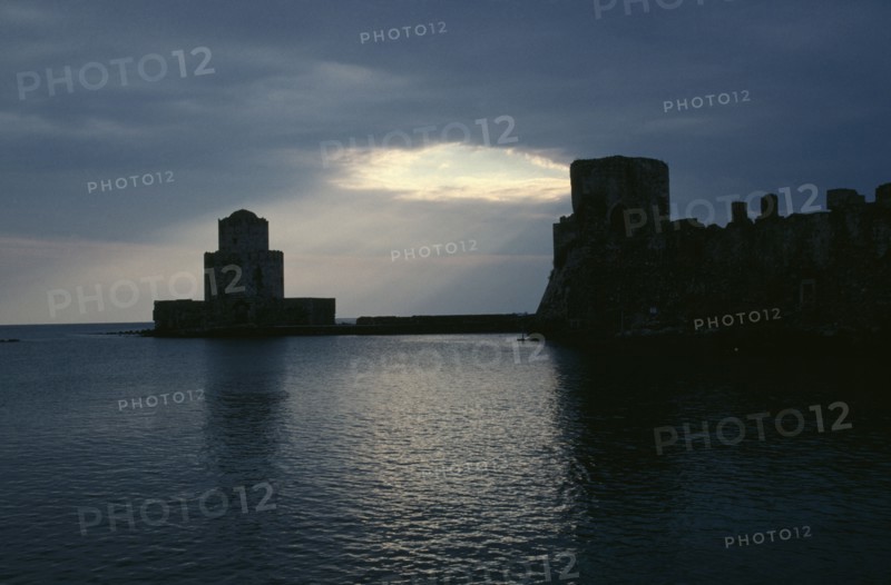 GREECE, Peloponnese, Methoni, View across the sea towards fortress ruins lit by evening sun rays coming through a break in the clouds.