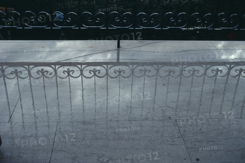 GREECE, Reflection, Decorative wrought iron balcony railings casting a shadow onto a pale wet floor.