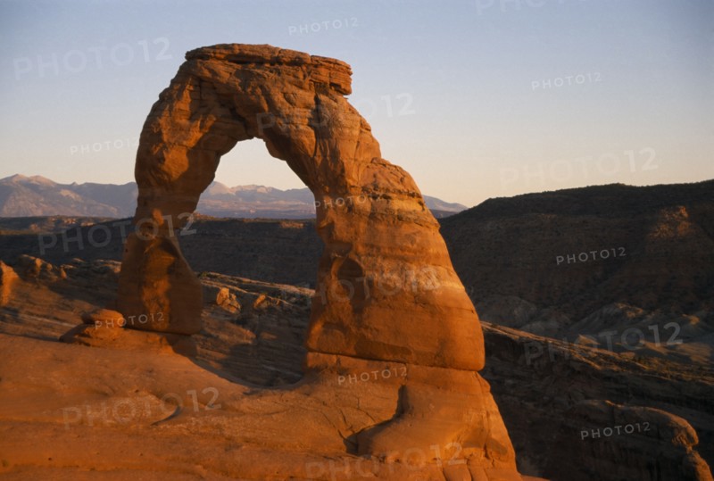 USA, Utah, Arches National Park, "Delicate Arch. Free standing, red cresent of rock at canyon edge. Mountainous landscape beyond. "