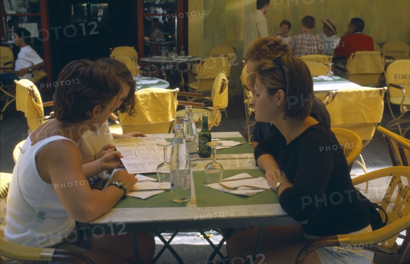 FRANCE, Provence-Cote d’Azur, Bouches-du-Rhône, "Arles.  Le Cafe La Nuit, Place du Forum.  Four young women seated at a table reading a menu. "