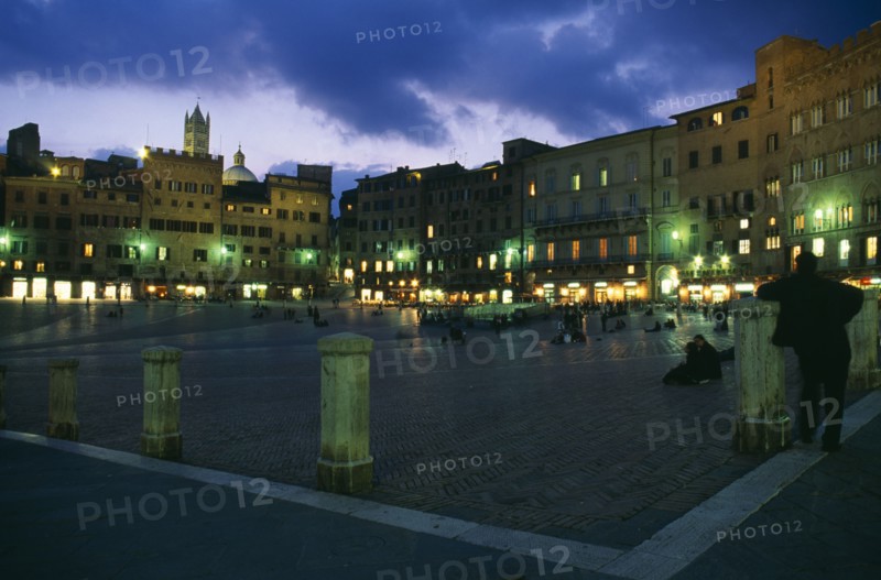 ITALY, Tuscany, Siena, Piazza del Campo.  Night view over Il Campo and cafes with people walking or sitting on the red brick paving.
